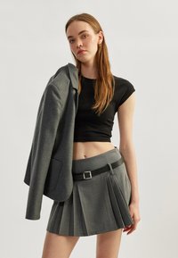 Blazer gris y falda gris con pliegues, con un cinturón negro, combinados con una blusa negra ajustada. Textura de tejido suave y diseño estructurado.
