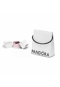 Sac de shopping blanc avec des poignées noires et le logo "PANDORA", à côté d'une petite boîte à bijoux blanche et rose avec le branding "PANDORA".
