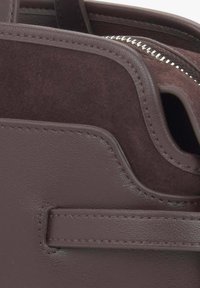 Bruine leren tas met een gladde afwerking, voorzien van suède accenten, een ritssluiting en zichtbare stiksels.