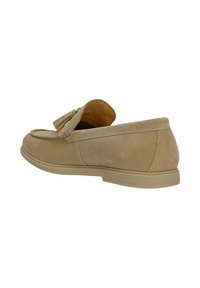Mocassin en daim beige avec détail pompon, talon bas et bout arrondi, présenté sous un angle latéral arrière sur fond blanc.