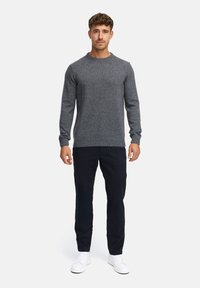 Grå genser med rund hals, ribbestrikkede mansjetter og hem, kombinert med mørke bukser og hvite sneakers, vist mot en nøytral bakgrunn.