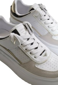 Sneaker bianchi e beige con dettagli perforati, accenti metallici e una suola spessa. Presenta linguetta e lacci con marchio.