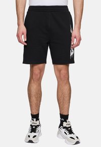 Svarta bomullsjersey-shorts med elastisk midja, rak passform och vitt grafiskt detalj på vänster sida.