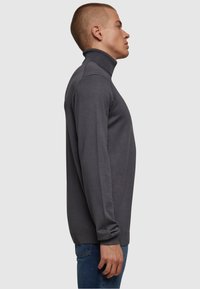 Dunkelgrauer Rollkragenpullover aus weichem Material, mit slim-Fit und gerippten Details am Kragen und an den Bündchen.