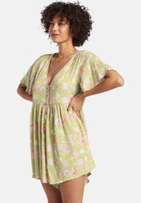 Vestido floral verde con un profundo escote en V, mangas acampanadas, cintura elástica y bolsillos laterales. Presenta patrones florales en rosa y azul.