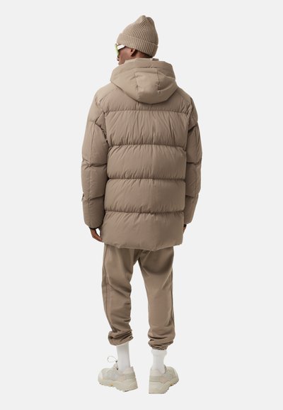 Puffer jacket in light beige with a hood, featuring horizontal quilted sections. Paired with matching beige joggers and white socks.
