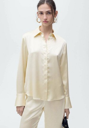 Cream satin blouse with a classic collar, button-down front, and long sleeves featuring wide cuffs. Paired with matching satin pants.