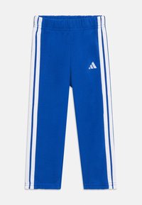 Niebieskie spodnie sportowe o miękkiej fakturze, elastycznym pasie, białych paskach po bokach oraz małym białym logo na lewej udzie.