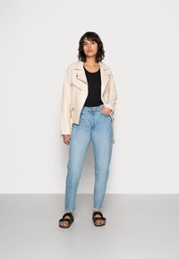 Šviesiai smėlinės spalvos odinė striukė su užtrauktukų detalėmis, juoda palaidinė, šviesiai mėlynos aukšto juosmens džinsai ir juodi sandalai su diržais.