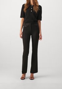 Czarna koszulka polo z trzema guzikami, w połączeniu z czarnymi spodniami z wysokim stanem, posiadającymi kieszenie i krój ze spódnicą. Gładka faktura.