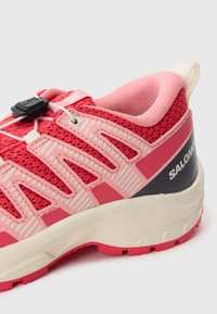 Red and pink athletic shoe with mesh fabric, striped accents, and a pull tab. Features a secure lace lock and a cushioned sole.