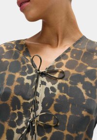 Leopardenmuster-Oberteil mit tiefem V-Ausschnitt, das mit einer gebundenen Akzentfarbe in Kontrastfarben verziert ist. Glattes Material mit sanftem Glanz und variierenden Musterdetails.