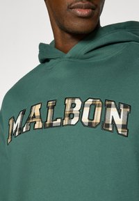 Πράσινο φούτερ με υφή στο ύφασμα. Διαθέτει τη λέξη «MALBON»  σε μεγάλα, πολυμορφικά γράμματα με σχέδιο καρό. Κανονική εφαρμογή με κουκούλα και κορδόνι.