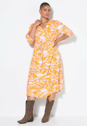 Vestido midi colorido en un patrón de camuflaje naranja y rosa, con un escote en V, mangas abullonadas y cintura ajustada, combinado con botas vaqueras marrones.