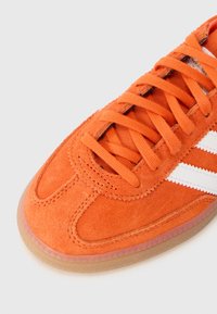 Sneaker in suede arancione con strisce bianche, con punta arrotondata, suola in gomma e lacci texturizzati. Accentuato da cuciture a contrasto.