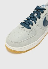 Vaaleanharmaa lenkkari, jossa on sileää nahkaa ja mokkanahkaa. Varustettu tummansinisillä nauhoilla, rei'itetyllä kärkiosalla ja kumipohjalla.