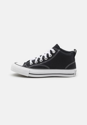 Zapatillas altas de lona negra con cordones blancos, puntera de goma y suela blanca con rayas negras y detalles de costura en contraste.