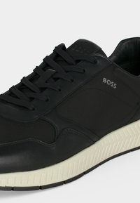 Baskets noires BOSS avec tige en tissu texturé et cuir, lacets noirs et semelle blanche rainurée.