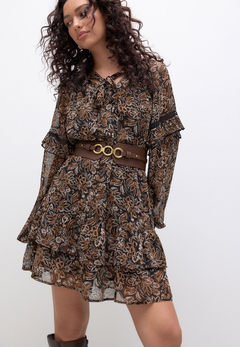 Robe marron à motif floral avec volants, manches longues et col noué. Associée à une ceinture marron avec des accents métalliques dorés.