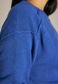 Kék kötött pulóver, puha tapintással, kerek nyakkivágással és finom varrási részletekkel a vállnál.