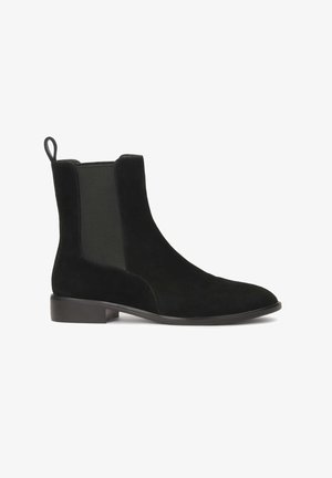 Stivale alla caviglia in suede nero con pannelli laterali elasticizzati e una linguetta. Caratterizzato da una punta arrotondata e un tacco basso e spesso. Contrasto di materiali texturizzati.