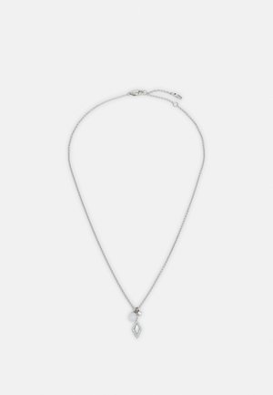 Collier en chaîne argentée avec un petit pendentif en forme de losange et deux petites breloques rondes sur un fond blanc uni.