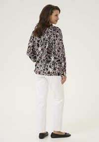 Lässig geschnittene schwarze Bluse mit rosa Blumenmuster, weiße Hose und schwarze Ballerinas. Glatte Stoffqualität; lange Ärmel und entspannter Schnitt.