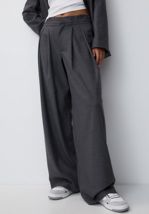 Grijze geplooide wijde broek gemaakt van gestructureerde stof, met een streepjespatroon en een hoge tailleband, gecombineerd met witte sneakers.