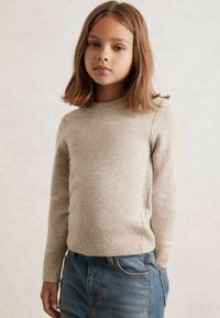 Maglione lavorato a maglia beige con scollatura rotonda, polsini e orlo a coste, caratterizzato da leggeri dettagli nelle cuciture laterali, abbinato a jeans in denim blu.