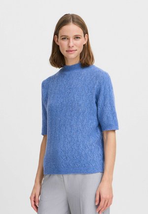 Hellblauer kurzärmeliger Strickpullover mit Wellenmuster, klassischem Rundhalsausschnitt und weicher, strukturierter Oberfläche. Kombiniert mit grauen Hosen.
