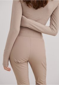 Beige langermet topp og høyt liv leggings. Leggingsene har glatt tekstur, tettsittende fasong og subtil merkingen på midjebåndet.