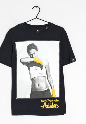 Czarny t-shirt Adidas z czarno-białym zdjęciem wysportowanej kobiety noszącej żółte owijki na ręce oraz tekstem "Risk Dare Win Adidas" w żółtym kolorze.