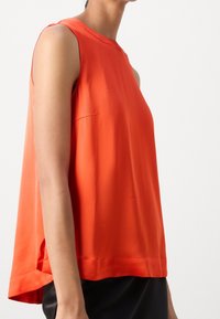 Top arancione senza maniche con vestibilità rilassata, realizzato in tessuto morbido. Le fessure laterali e il collo rotondo aggiungono un tocco al suo design minimalista.
