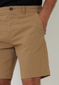 Shorts beiges en tissu coton mélangé, avec une taille plate, des poches latérales, des passants de ceinture et une fermeture à un bouton.