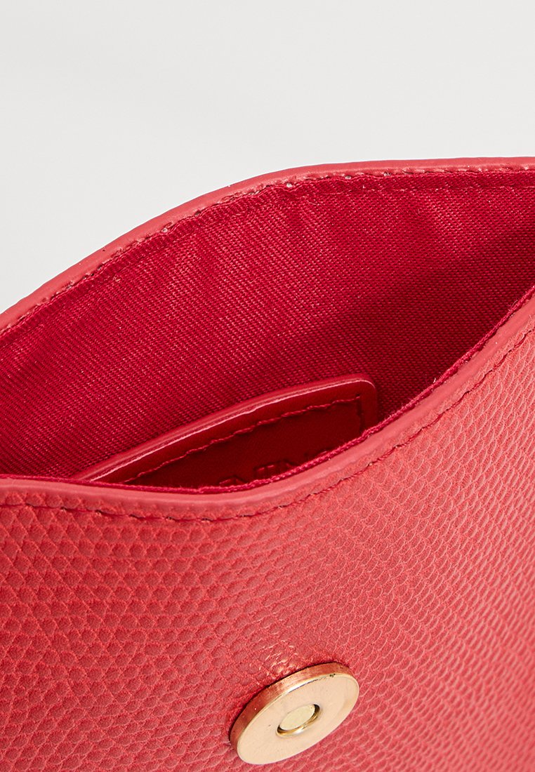 Primer plano de una cartera de cuero roja texturizada abierta con un botón a presión dorado y forro interior de tela visible.