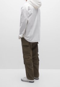 Sudadera blanca con capucha y un corte relajado, combinada con pantalones cargo verde oliva que cuentan con múltiples bolsillos y una textura de tela duradera. Zapatillas blancas.