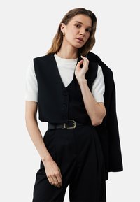 Zwarte vest over een wit shirt met korte mouwen, voorzien van een v-hals en knopen. Gecombineerd met hoge zwarte broek en een zwarte riem met een gouden gesp.