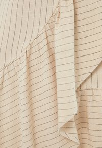 Tela beige con finas rayas negras horizontales; presenta un borde rizado y una textura suave. El diseño exhibe formas superpuestas y en capas.