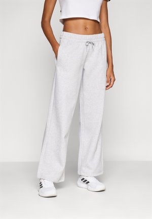 Personne portant un pantalon de survêtement gris clair à jambes larges avec taille élastique et cordon, un top court blanc et des baskets blanches Adidas.