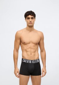 Black cotton boxer briefs with a white "CALVIN KLEIN" logo on the waistband. The fit is snug, and the fabric appears smooth and stretchy.