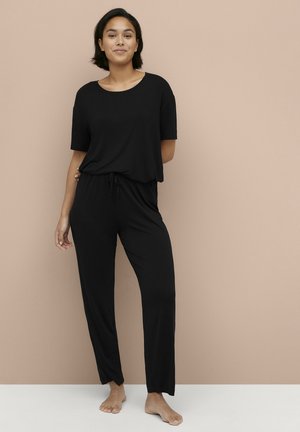 Ensemble de loungewear noir comprenant un haut à manches courtes ample et un pantalon à cordon de serrage, fabriqué dans un tissu doux avec une texture lisse.