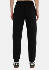 Pantaloni sportivi neri con vita elasticizzata, polsini aderenti e una texture liscia, abbinati a sneaker bianche e verdi.