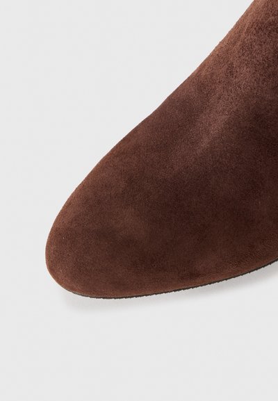 Ruskea mokkanahkainen nilkkuri, jossa on terävä kärki, sileä pinta ja matala, tasapohjainen pohja. Painota yläosan materiaalia ja kärjen muotoa.