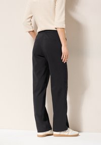 Black, wide-leg pants with a smooth texture, elastic waistband, and two back pockets. Paired with light-colored sneakers.