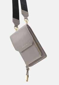 Szara skórzana torebka na przekątną z magnetycznym klapem, złotym zamkiem błyskawicznym i regulowanym czarnym paskiem. Posiada dekoracyjny frędzel i detal z logo.