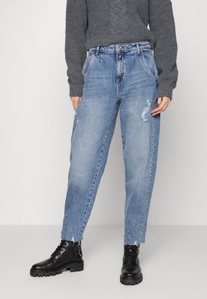 Frau trägt hellblaue Jeans mit hoher Taille und Knöchelschlitzen, einen grauen Strickpullover und schwarze Schnür-Kampfstiefel.