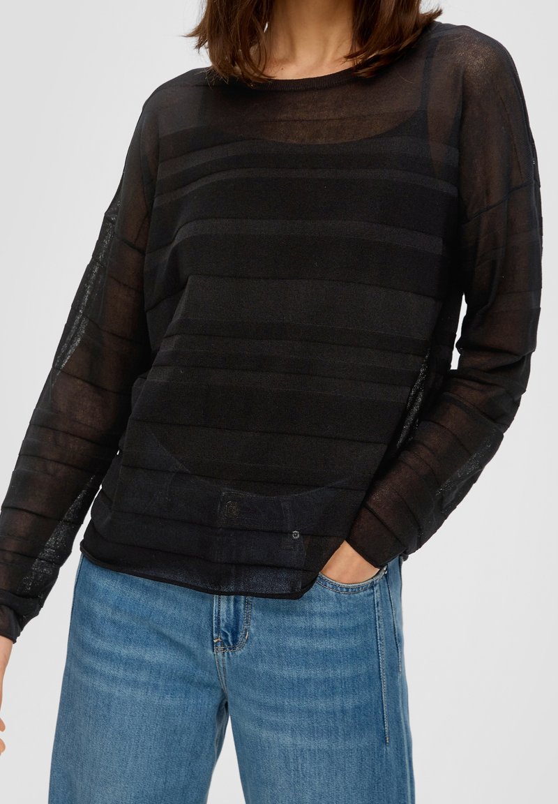 Top noir à manches longues en tissu transparent à rayures horizontales. Présente un col rond, une coupe décontractée et un détail poche. Associé à un jean bleu.