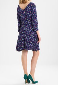 Floral print dress in navy with three-quarter sleeves, a V-neckline, and a flared skirt. Paired with green high-heeled shoes.
