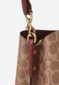 Brown fabric handbag with circular patterns, accented by a burgundy leather strap and gold-tone hardware at the attachment point.