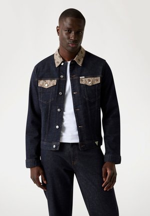 Chaqueta de denim en azul oscuro con un cuello beige estampado, con botones a presión, dos bolsillos en el pecho y detalles de costura en contraste.